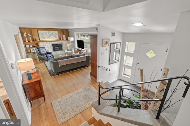 foyer with a stone fireplace, baseboards, wood finished floors, vaulted ceiling, and visible vents