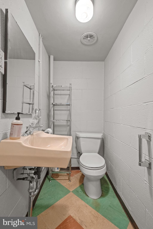 bathroom featuring visible vents, concrete block wall, and toilet