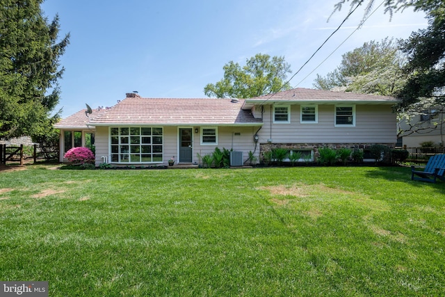 rear view of property with a lawn, central AC, fence, and a chimney