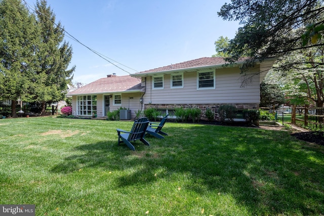 rear view of property featuring a lawn, fence, stone siding, and cooling unit