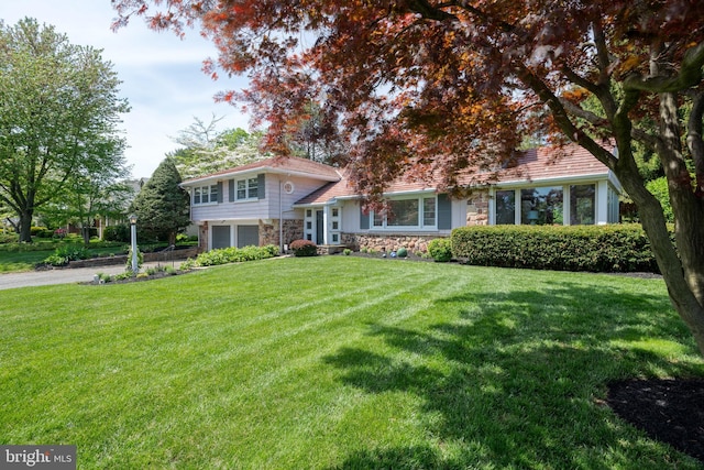 split level home with a garage, a front lawn, driveway, and stone siding
