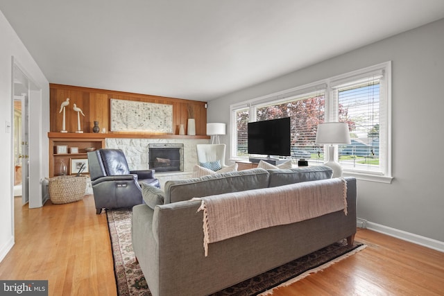 living area with light wood-style floors, baseboards, and a stone fireplace