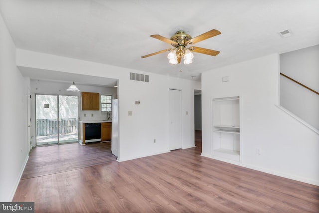 unfurnished living room with a sink, a ceiling fan, baseboards, wood finished floors, and visible vents