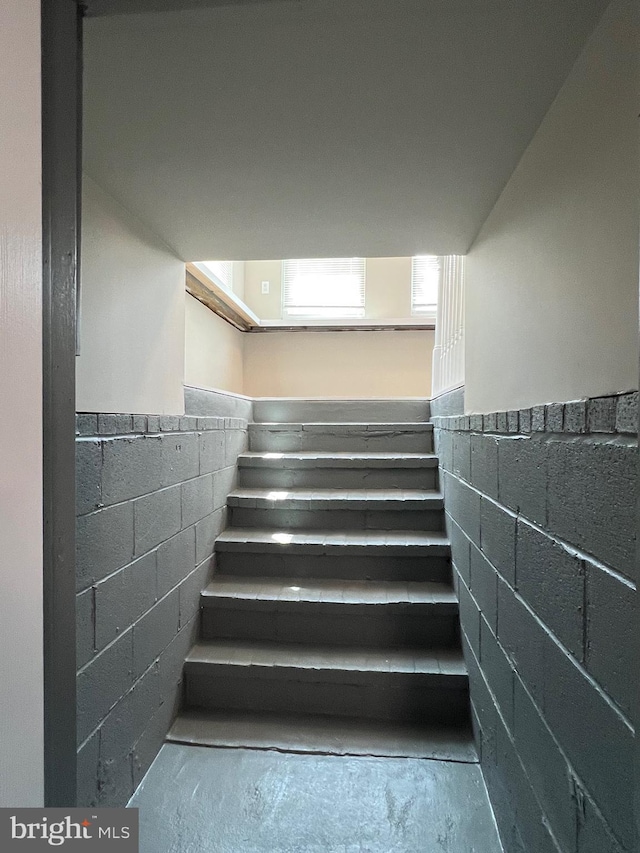 1948 Victory Dr, Baltimore, MD 21227 - staircase featuring wainscoting, concrete block wall, and unfinished concrete flooring