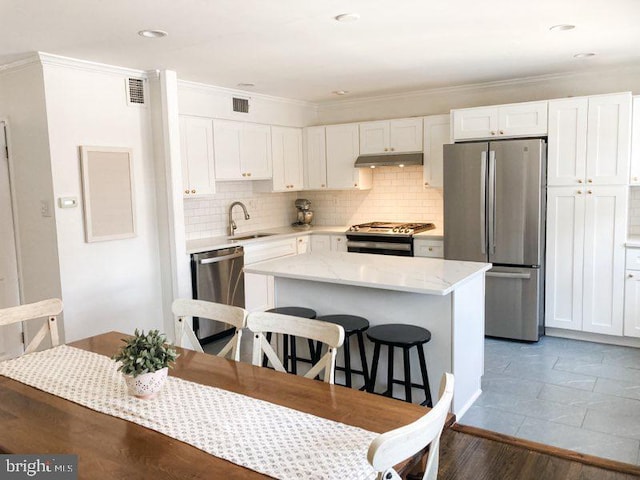 kitchen with a sink, under cabinet range hood, a breakfast bar, stainless steel appliances, and white cabinetry