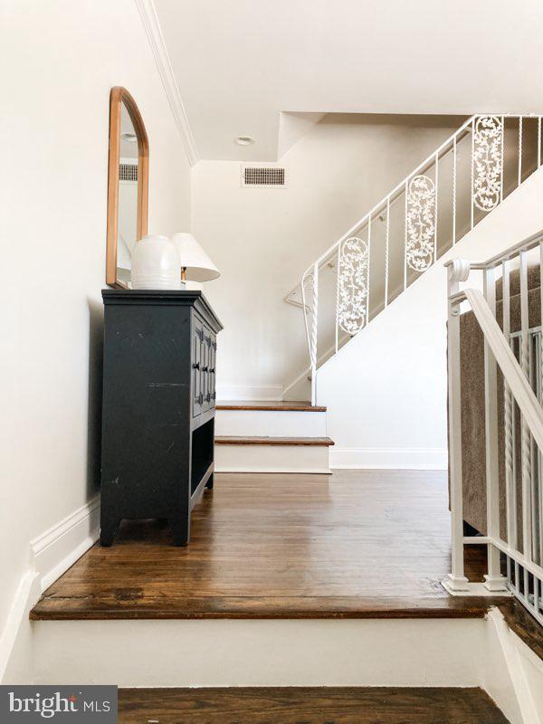 staircase featuring baseboards, visible vents, ornamental molding, and wood finished floors