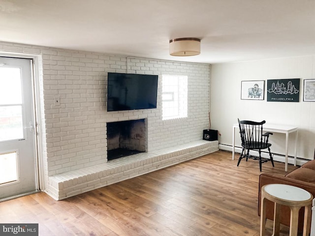 living area with brick wall, baseboard heating, a brick fireplace, and wood finished floors