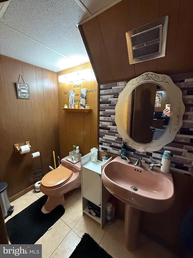 half bath with tile patterned floors, visible vents, toilet, and wood walls