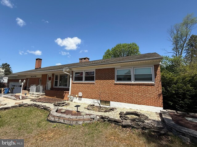 rear view of house featuring a chimney, a garage, and brick siding