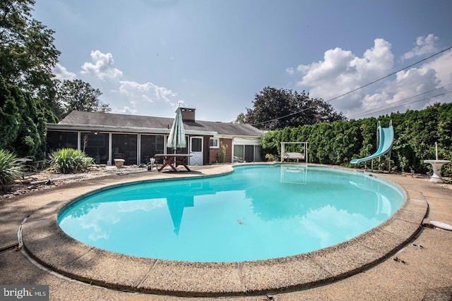 outdoor pool with a water slide and a sunroom