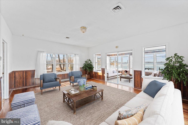 living area with a baseboard radiator, wood finished floors, a wainscoted wall, and visible vents