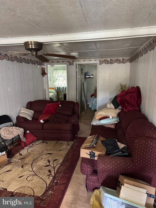 living area with ceiling fan, wooden walls, and carpet