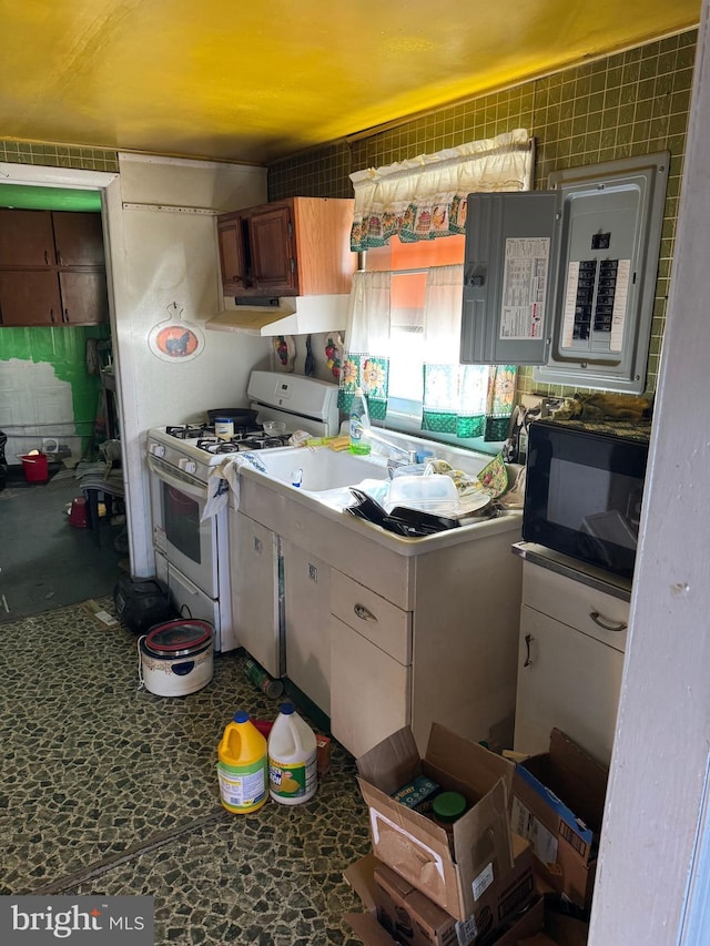 kitchen with under cabinet range hood, electric panel, white gas stove, black microwave, and dark countertops