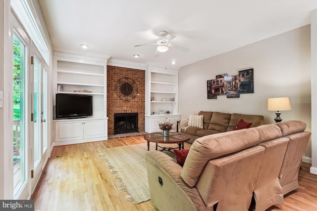 living area featuring ceiling fan, light wood finished floors, built in features, and a brick fireplace
