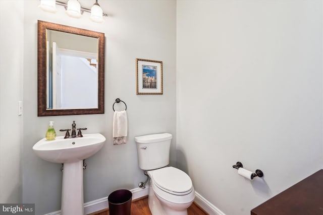 half bath featuring wood finished floors, toilet, and baseboards