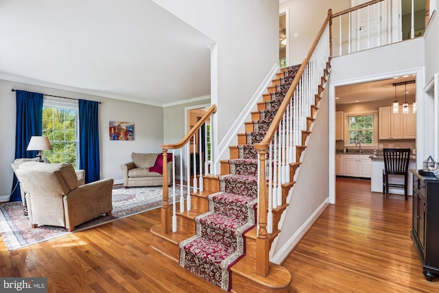 stairway featuring wood finished floors, plenty of natural light, ornamental molding, and baseboards