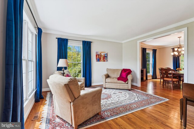 living area with crown molding, an inviting chandelier, wood finished floors, and baseboards