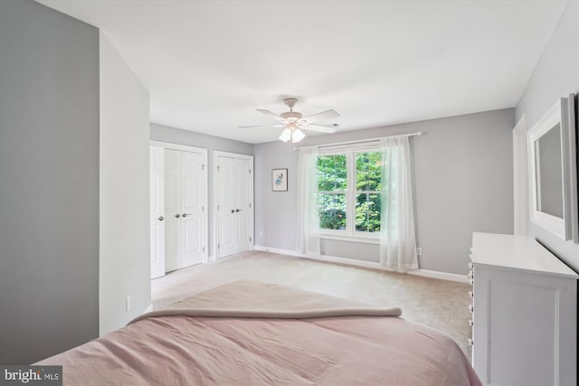 bedroom with two closets, ceiling fan, baseboards, and light carpet