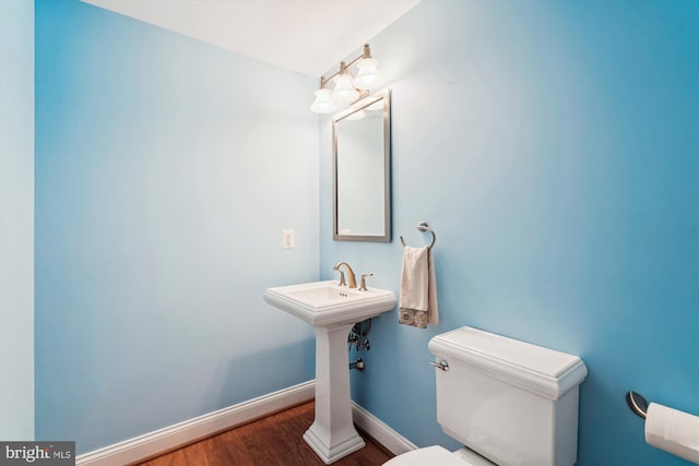 half bath featuring baseboards, wood finished floors, toilet, and a sink