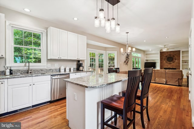 kitchen with stainless steel dishwasher, white cabinets, a sink, light wood finished floors, and a fireplace