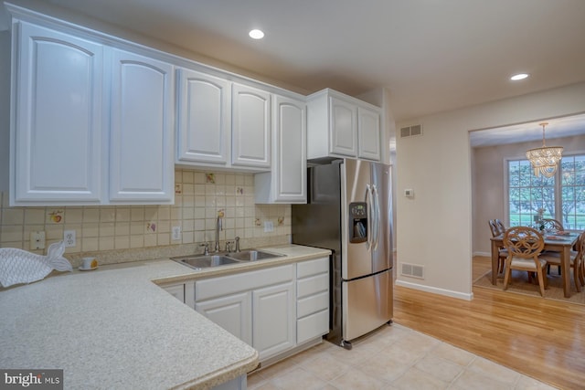 kitchen featuring stainless steel refrigerator with ice dispenser, a sink, a chandelier, white cabinets, and light countertops