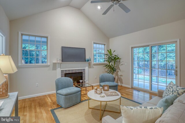 living area with a tile fireplace, wood finished floors, high vaulted ceiling, ceiling fan, and baseboards