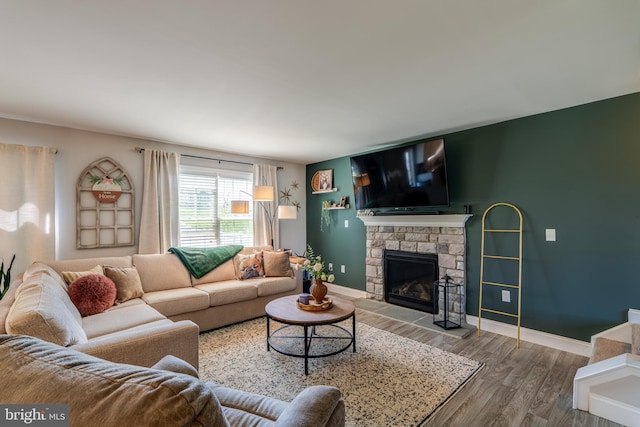 living room with baseboards, a stone fireplace, and wood finished floors