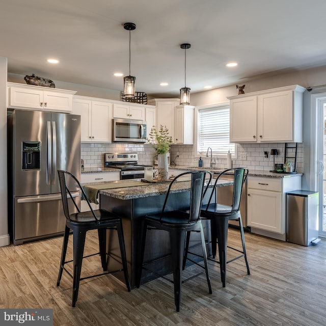 kitchen featuring white cabinets, a kitchen breakfast bar, appliances with stainless steel finishes, and light wood-style flooring