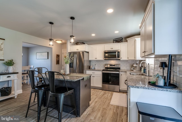 kitchen featuring a breakfast bar area, backsplash, appliances with stainless steel finishes, a sink, and light stone counters