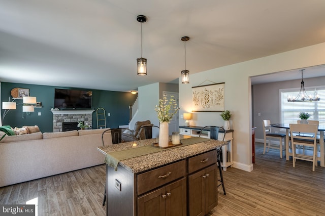 kitchen featuring a kitchen island, a kitchen bar, a stone fireplace, pendant lighting, and light wood-style flooring