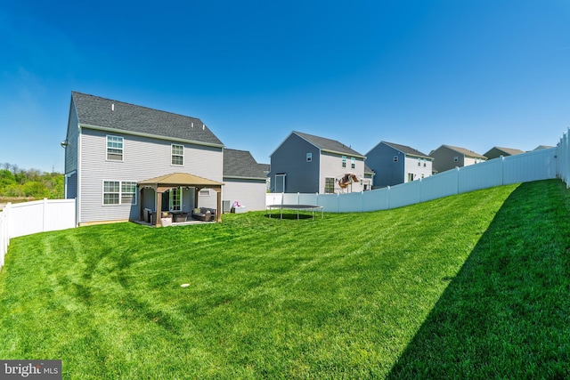 back of house featuring a fenced backyard, a trampoline, a gazebo, and a yard