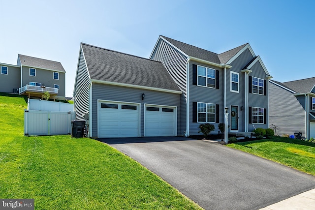 colonial home with a front lawn, fence, a gate, an attached garage, and driveway