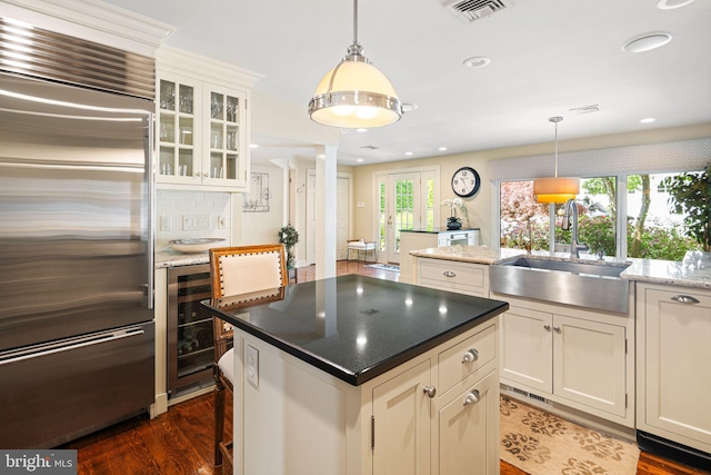 kitchen featuring stainless steel built in refrigerator, a sink, a center island, dark wood-style flooring, and beverage cooler