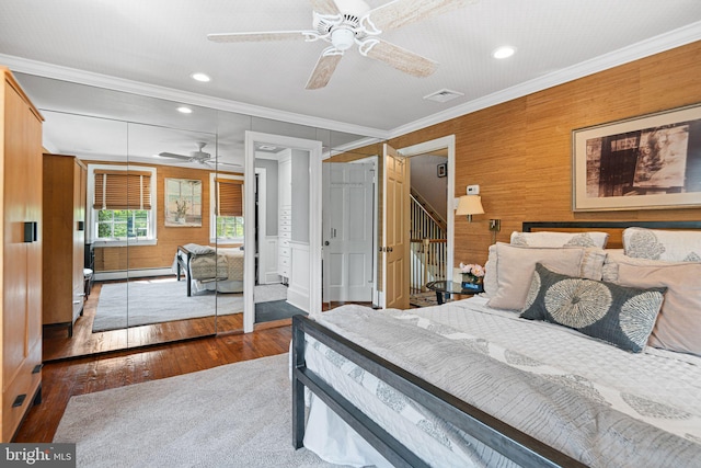 bedroom with hardwood / wood-style flooring, a baseboard heating unit, crown molding, recessed lighting, and wood walls