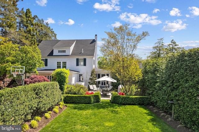 rear view of property with a chimney, a yard, and a patio