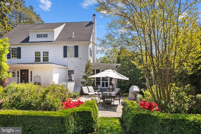 back of house with a chimney, a patio area, and a shingled roof