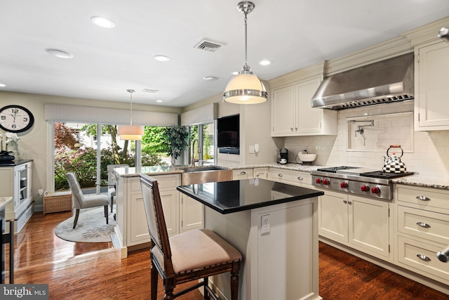 kitchen featuring stainless steel gas stovetop, wall chimney range hood, a sink, backsplash, and a kitchen island