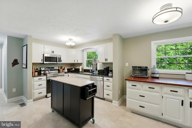 kitchen featuring a kitchen island, baseboards, white cabinetry, a sink, and stainless steel appliances