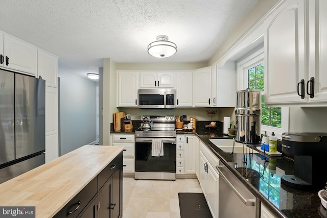 kitchen featuring a textured ceiling, wooden counters, stainless steel appliances, and white cabinetry