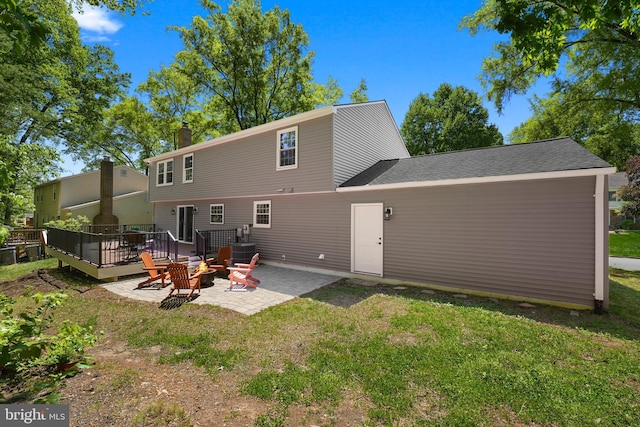 back of property featuring a lawn, a fire pit, a wooden deck, and a patio