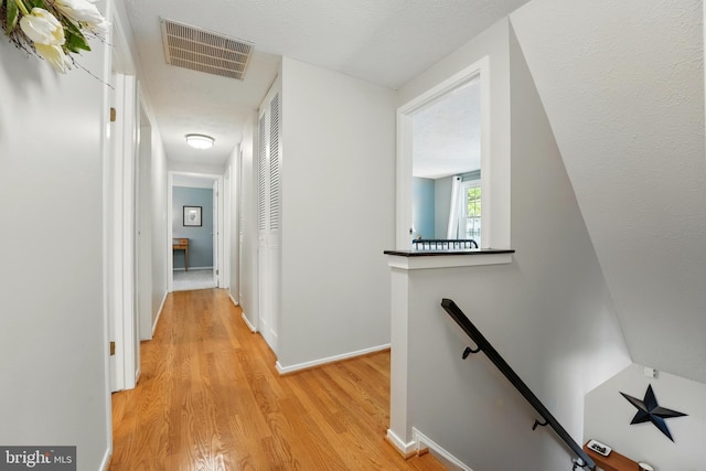 hallway with visible vents, baseboards, an upstairs landing, and light wood-type flooring