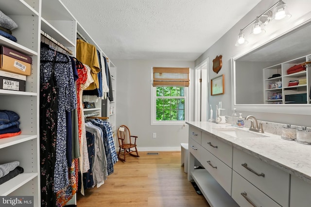 spacious closet featuring a sink, light wood-style floors, and visible vents
