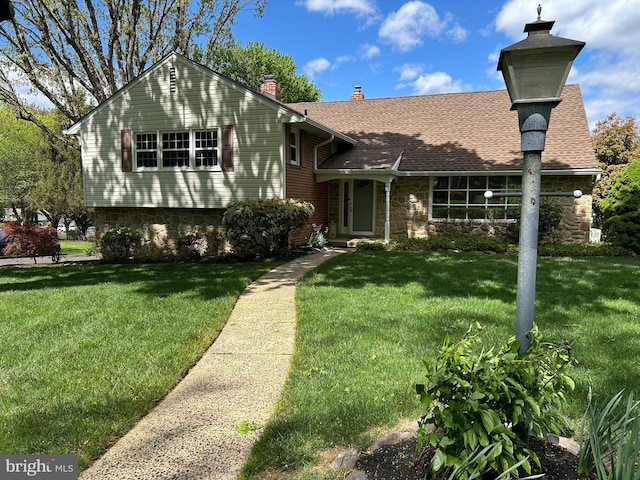 tri-level home featuring a front yard, stone siding, a shingled roof, and a chimney