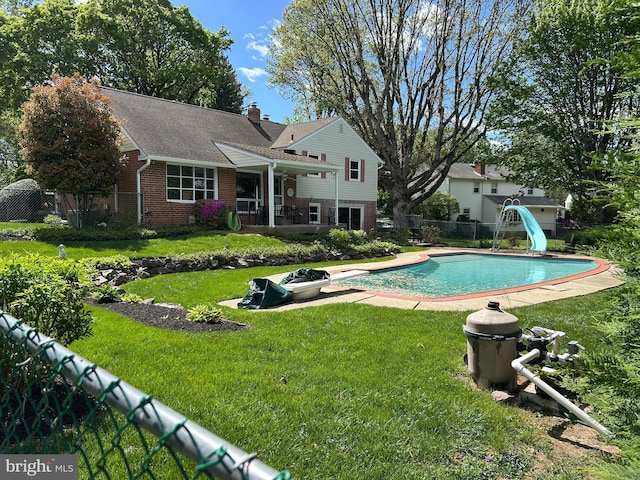 pool with a water slide, fence, and a yard