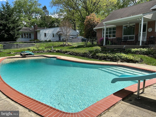 outdoor pool with a diving board, ceiling fan, a water slide, and fence
