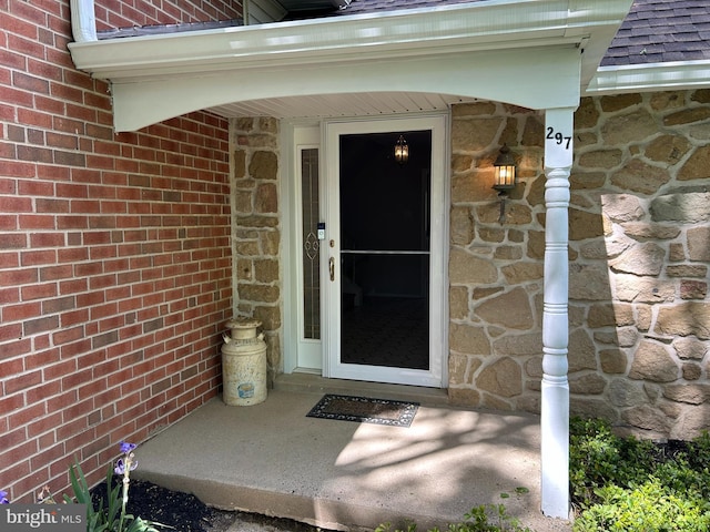 doorway to property featuring brick siding, a shingled roof, and stone siding