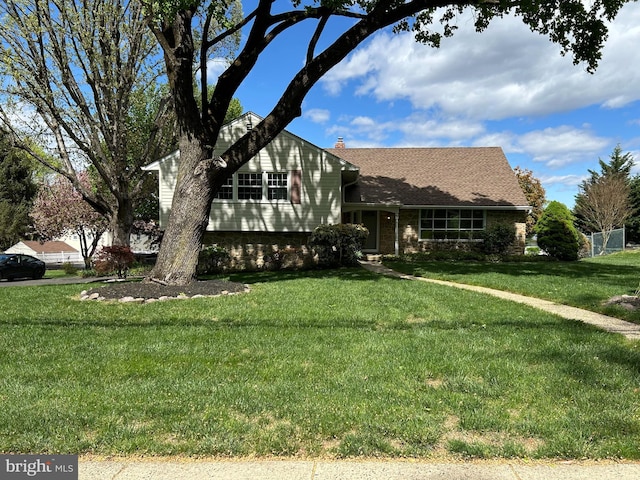 split level home featuring a chimney, a front yard, and brick siding