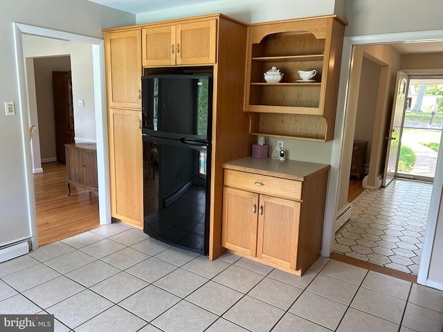 kitchen with light tile patterned flooring, a baseboard radiator, freestanding refrigerator, and light countertops