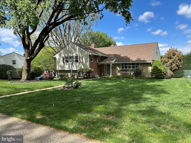 tri-level home with a front yard, stone siding, and a chimney