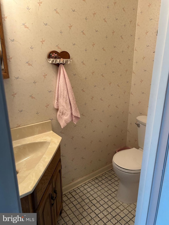 half bathroom with wallpapered walls, toilet, and vanity